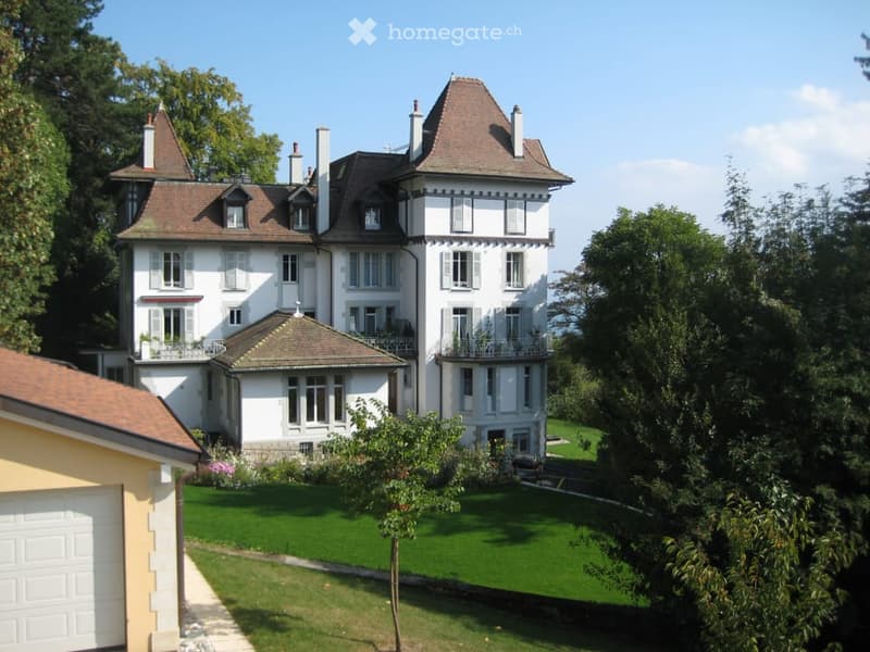 A large, elegant white mansion with multiple stories, dormer windows, and a well-maintained garden.