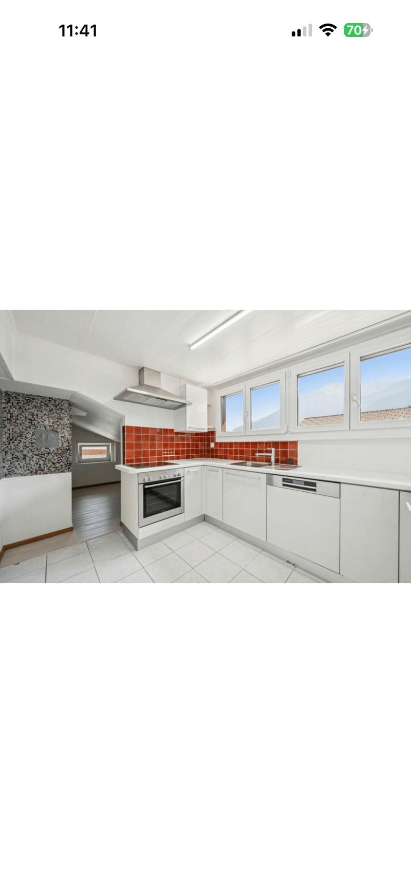 Modern kitchen with white cabinets, stainless steel appliances, and a tiled backsplash. Features an oven, sink, dishwasher, and ample natural light from large windows.