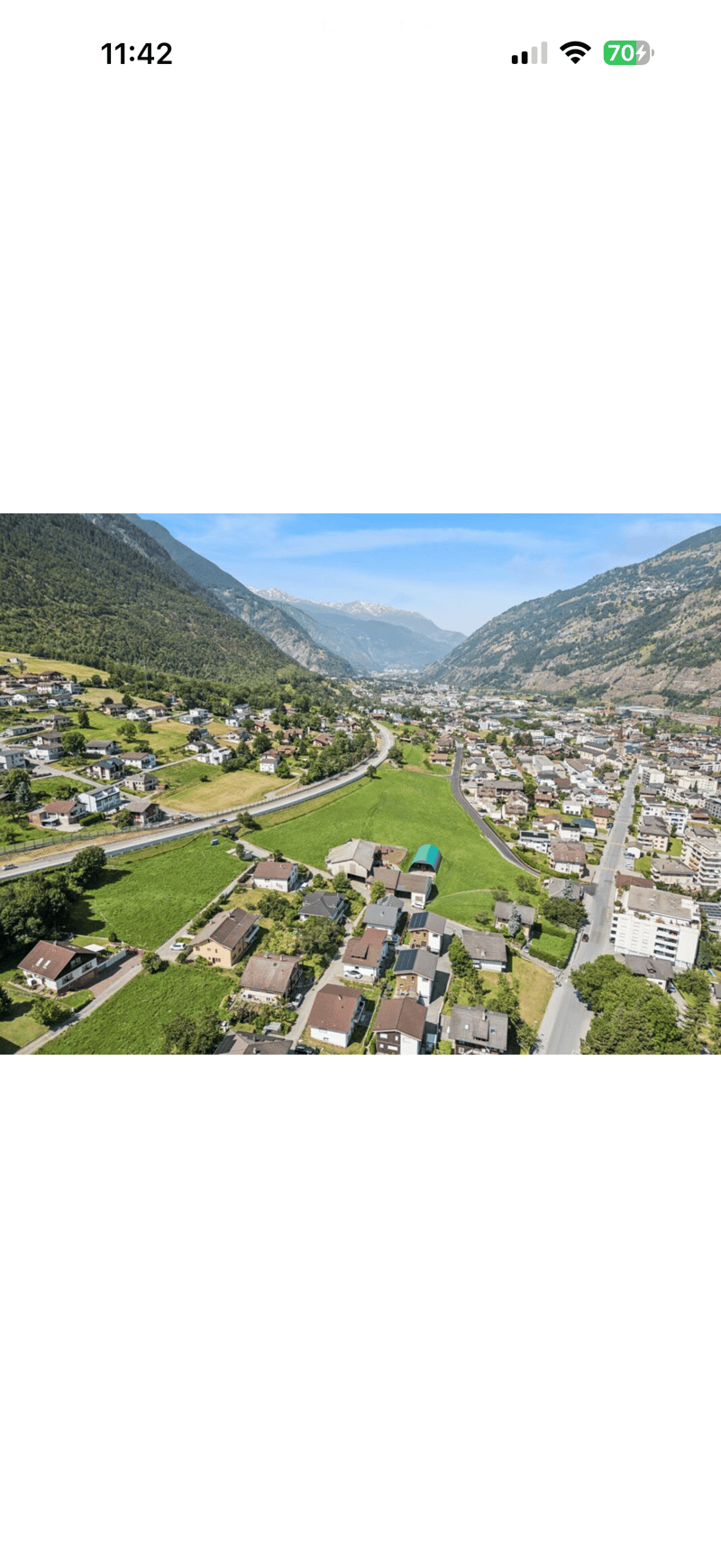 Aerial view of a small village nestled in a valley surrounded by mountains, featuring houses, roads, and green fields.
