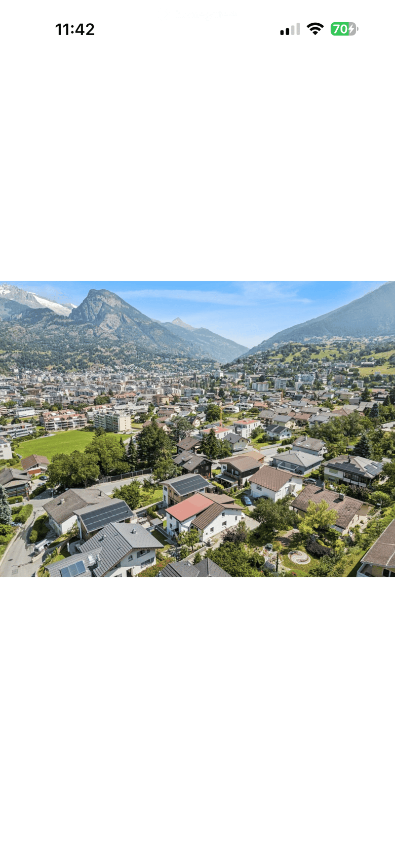 Aerial view of a town nestled in a valley surrounded by mountains, featuring houses, roads, and green spaces.