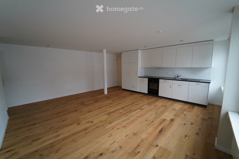 Empty room with light wooden flooring and white cabinetry along one wall, including a sink, stove, and countertop.