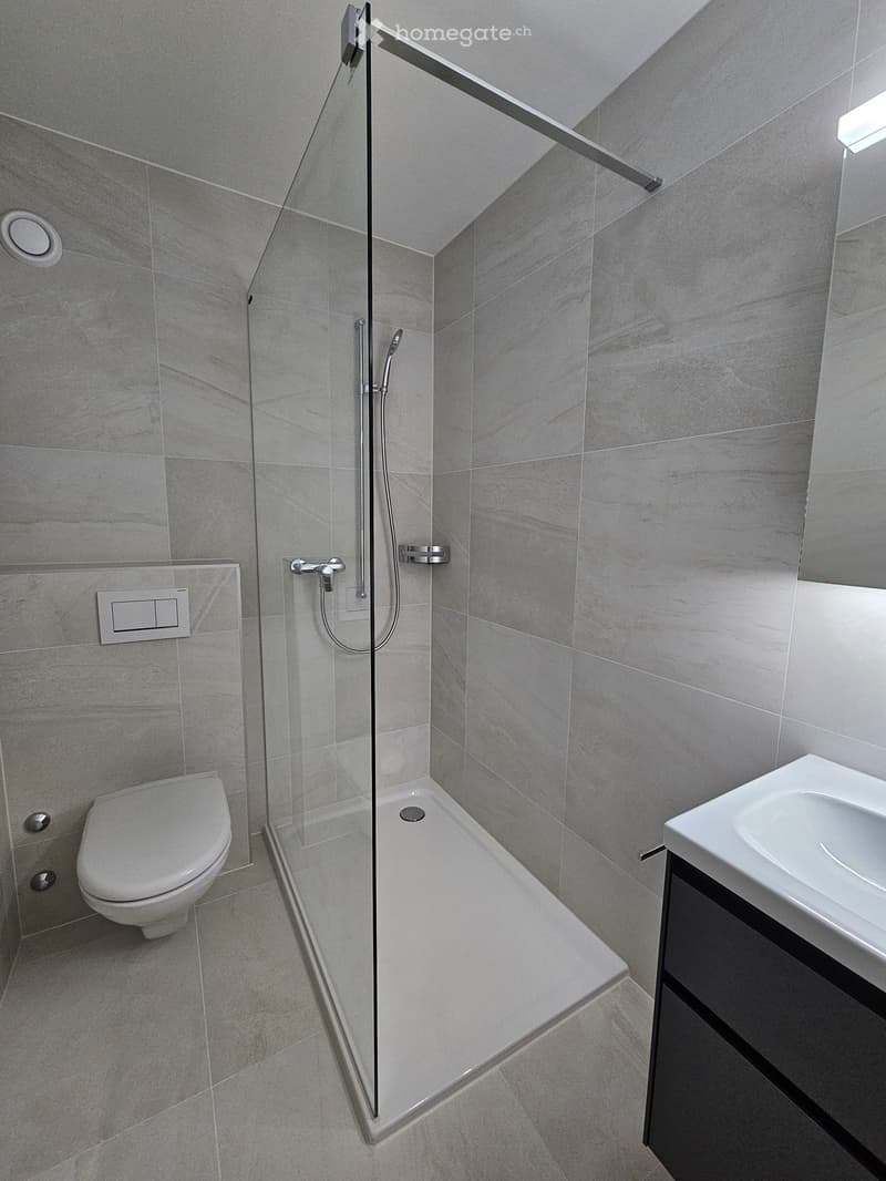 Shower with shower head, toilet, sink, cabinet, white floor and walls, glass partition, shower wall switches