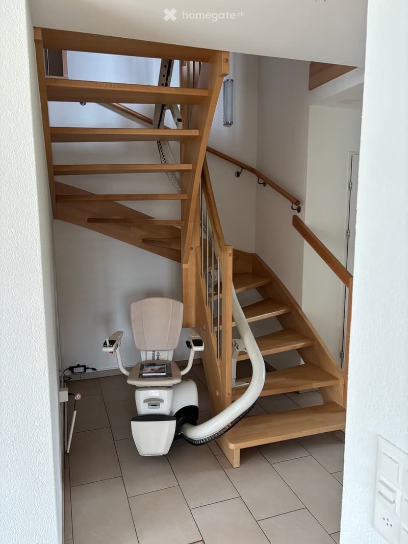 Staircase with wooden steps and handrails, featuring a white stair lift on the left side.