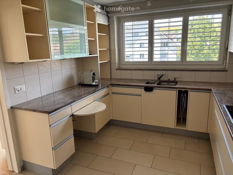 Modern kitchen with light-colored cabinets, granite countertops, and a sink with a faucet. A coffee maker is placed on the counter.