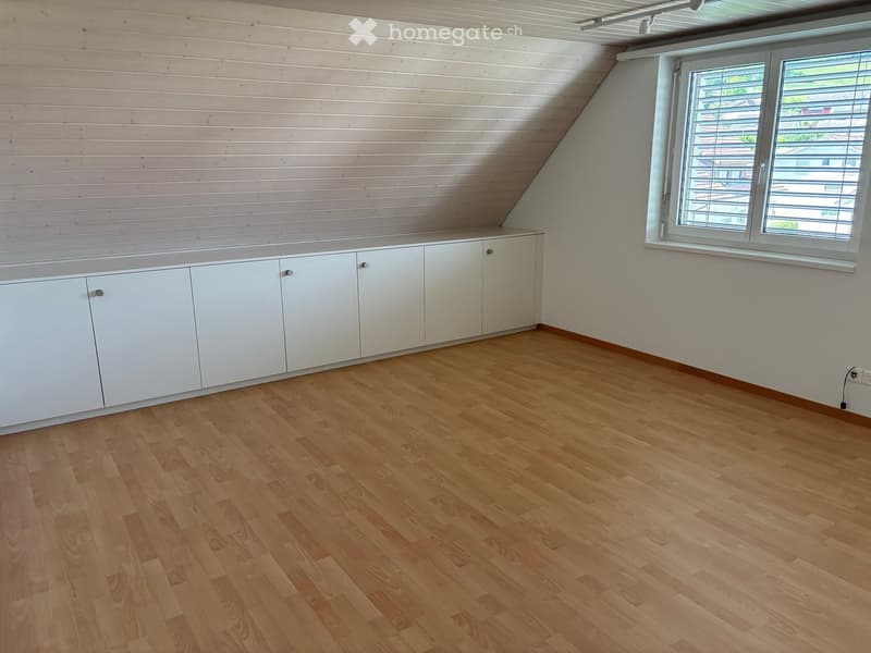 Empty room with wooden flooring, white cabinetry along one wall, and a large window with blinds.