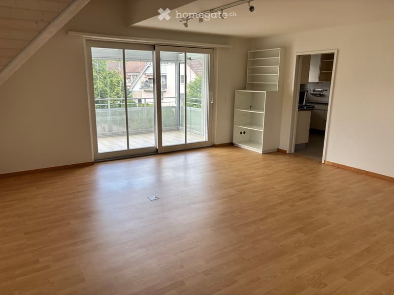 Empty room with wooden flooring, large sliding glass doors leading to a balcony, and built-in white shelving units.