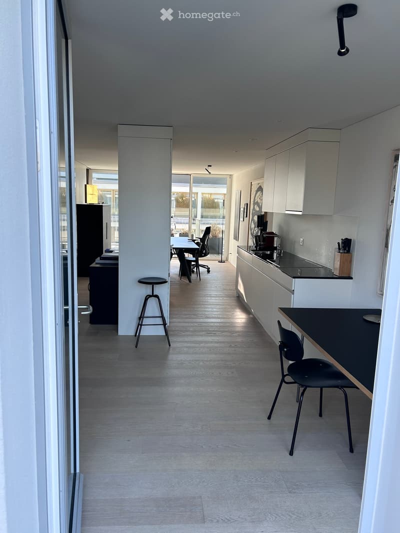 Modern, open-plan kitchen and dining area with light wood flooring, white cabinets, and a black dining table with chairs.