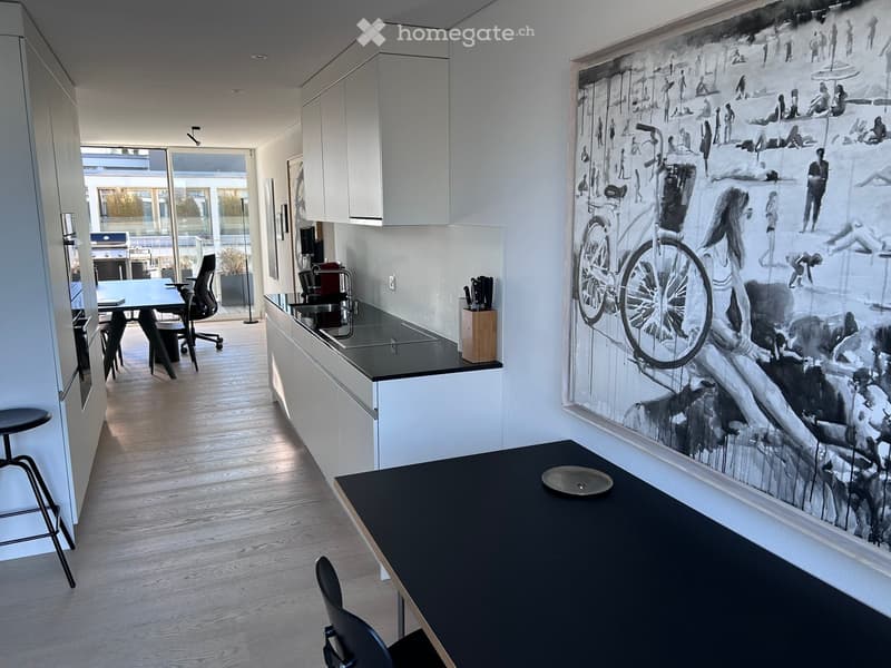 Modern kitchen with white cabinets, black countertops, and a large black-and-white mural on the wall. Includes a dining area with a black table and chairs, a kitchen island, and a small office area with a desk and chair.