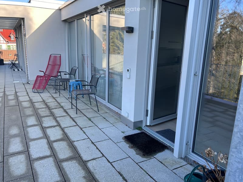 Balcony with tiled floor, large glass sliding doors, several chairs and a small table, and a potted plant near the entrance.