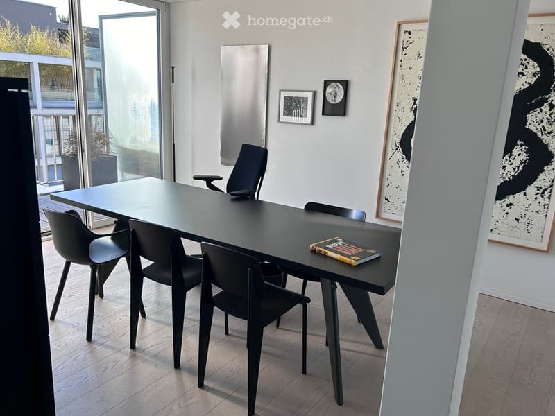 Modern dining area with a sleek black table, four black chairs, and a book on the table. Large windows and artwork on the walls.