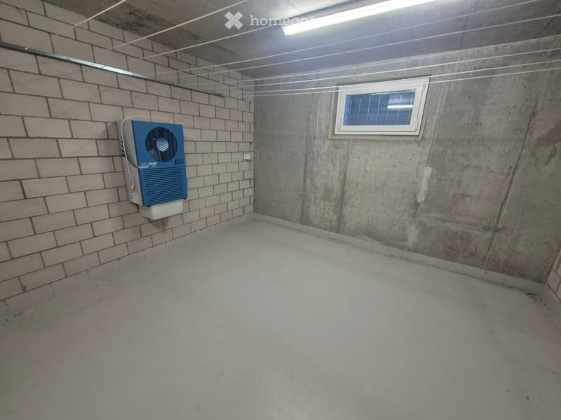 Empty room with concrete walls and floor, a small window, and a blue air conditioning unit mounted on one wall.