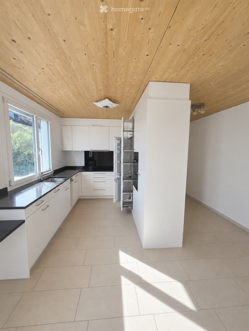 Modern, minimalist kitchen with white cabinets, black countertops, and a stainless steel sink. The space features a sleek, open design with a tall pantry unit and ample natural light from large windows.