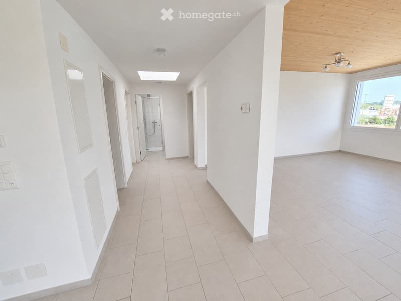 Empty hallway with white walls, tiled floor, and several doors leading to rooms. A window on the right side offers a view of the outside.
