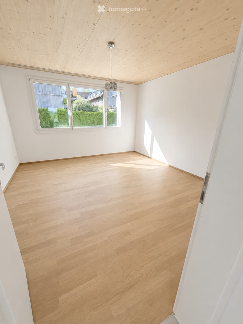 Empty room with light wooden flooring, white walls, and large windows letting in natural light. The ceiling is also made of light wood.