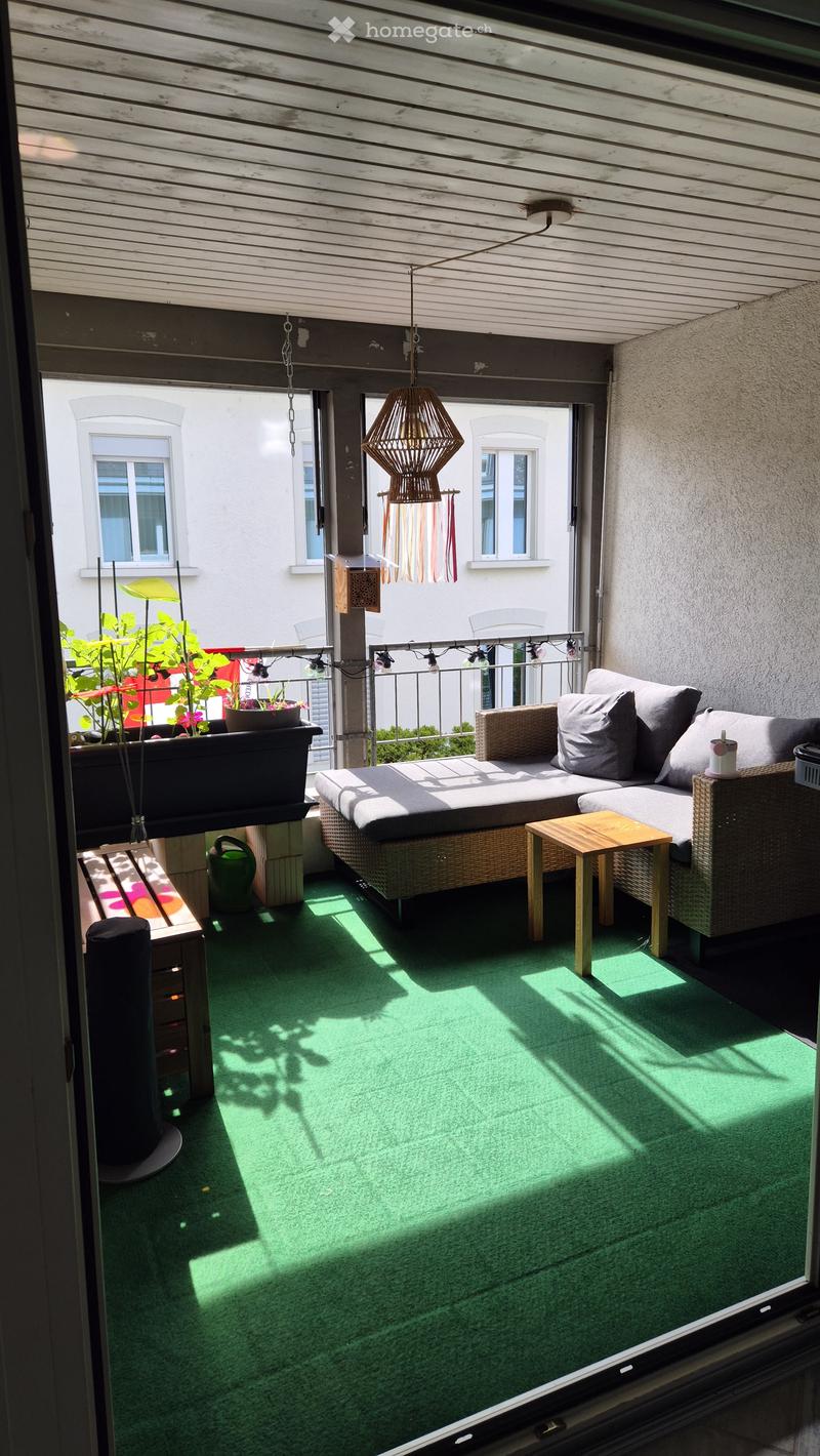 Balcony with green artificial turf, wooden decking, sofa, small table, and potted plants.