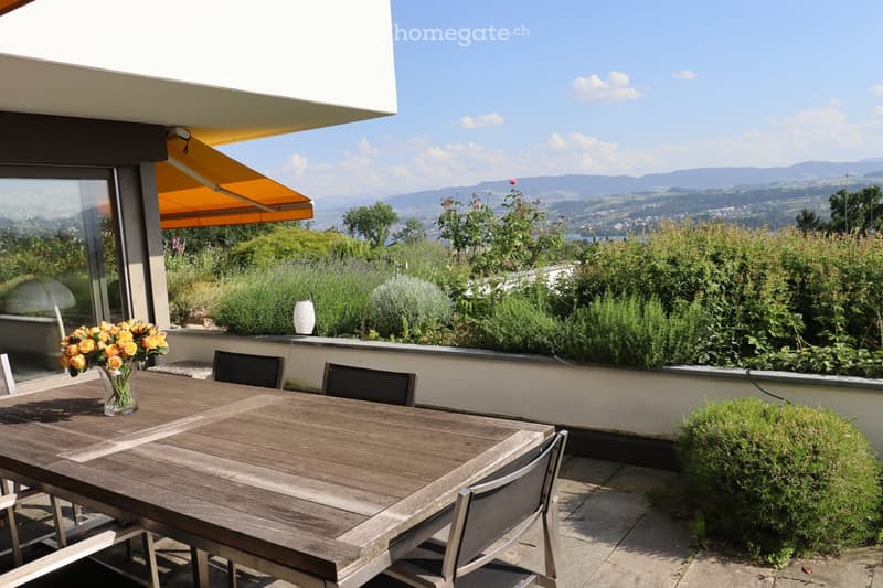 Balcony with wooden table, chairs, vase of flowers, and a view of the mountains.