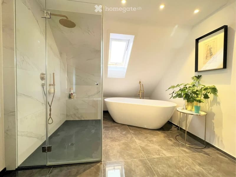 Modern bathroom with a freestanding bathtub, glass-enclosed shower, small round table with plant, and a framed mirror on the wall.
