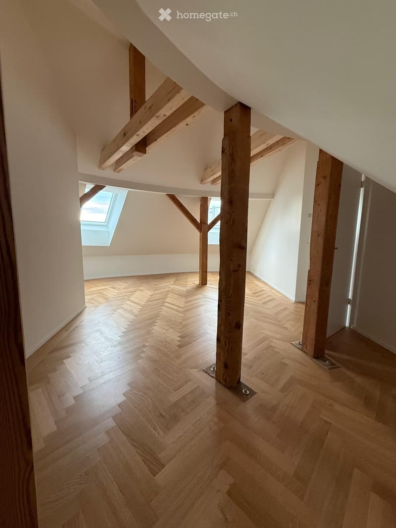 Empty attic space with wooden beams, herringbone parquet flooring, and skylight windows.