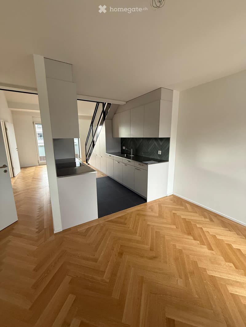 Modern kitchen with light grey cabinets, a central island, and herringbone wooden flooring.