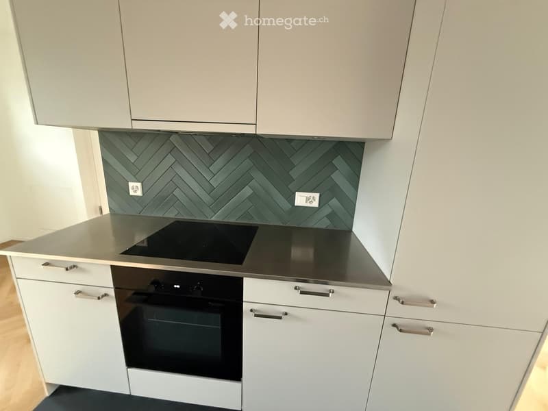 Modern kitchen with white cabinets, grey herringbone backsplash, induction cooktop, and built-in oven.