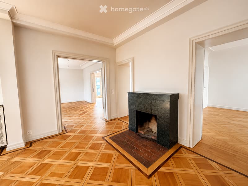 Empty hallway with wooden flooring, white walls, and a fireplace in the center. The hallway features multiple doorways leading to other rooms.