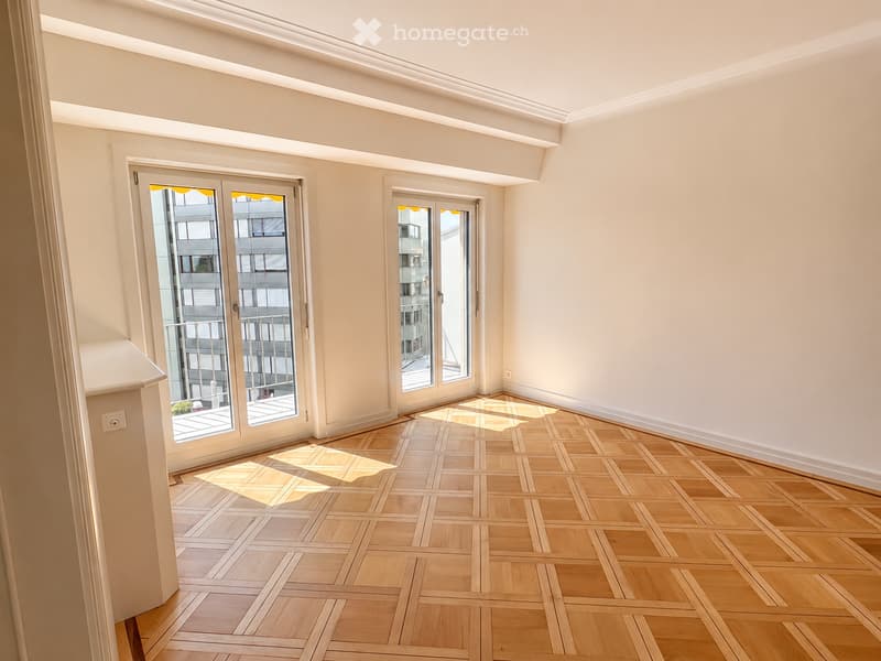 Empty room with light wooden parquet flooring, white walls, and large glass doors leading to a balcony area.