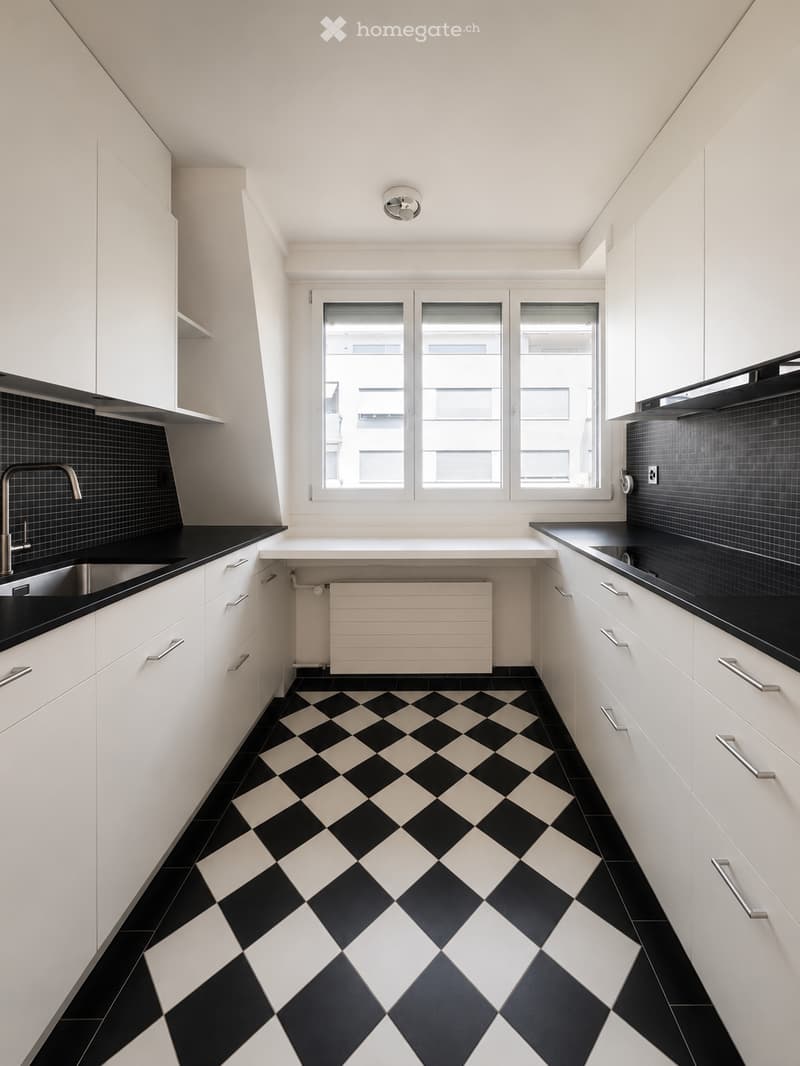 Modern kitchen with white cabinets, black countertops, and a black and white checkered floor. Features a sink, faucet, and radiator.