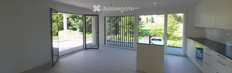 Empty kitchen with white cabinets, tiled floor, and large sliding glass doors opening to a garden area.