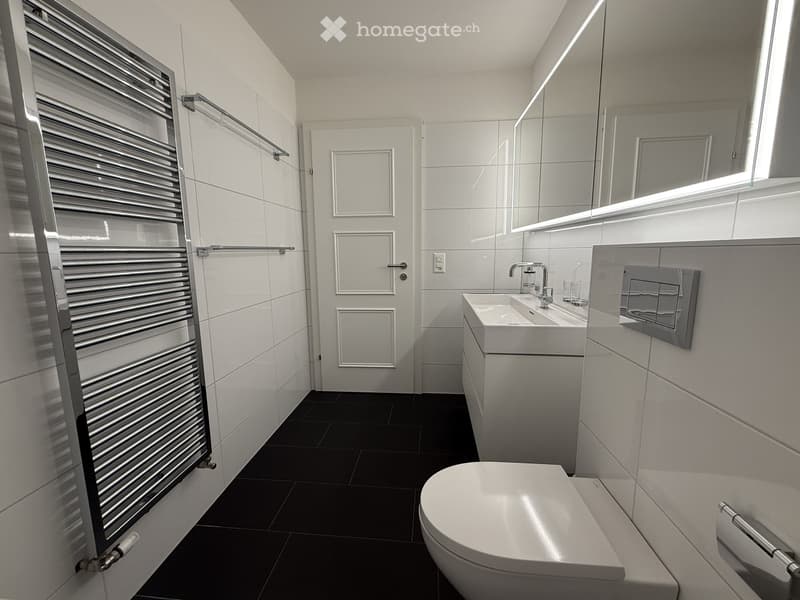 modern bathroom, white tiles, black floor, white sink, silver faucet, white toilet, silver towel rack