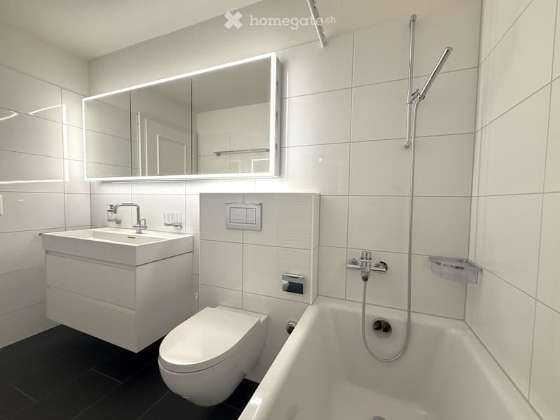 modern bathroom with white tiles, white sink, white toilet, bathtub, mirror, shower head