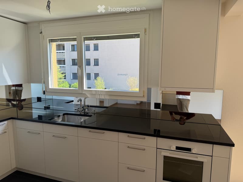modern kitchen with white cabinets, black countertops, stainless steel sink, faucet, oven, window with view of the outside