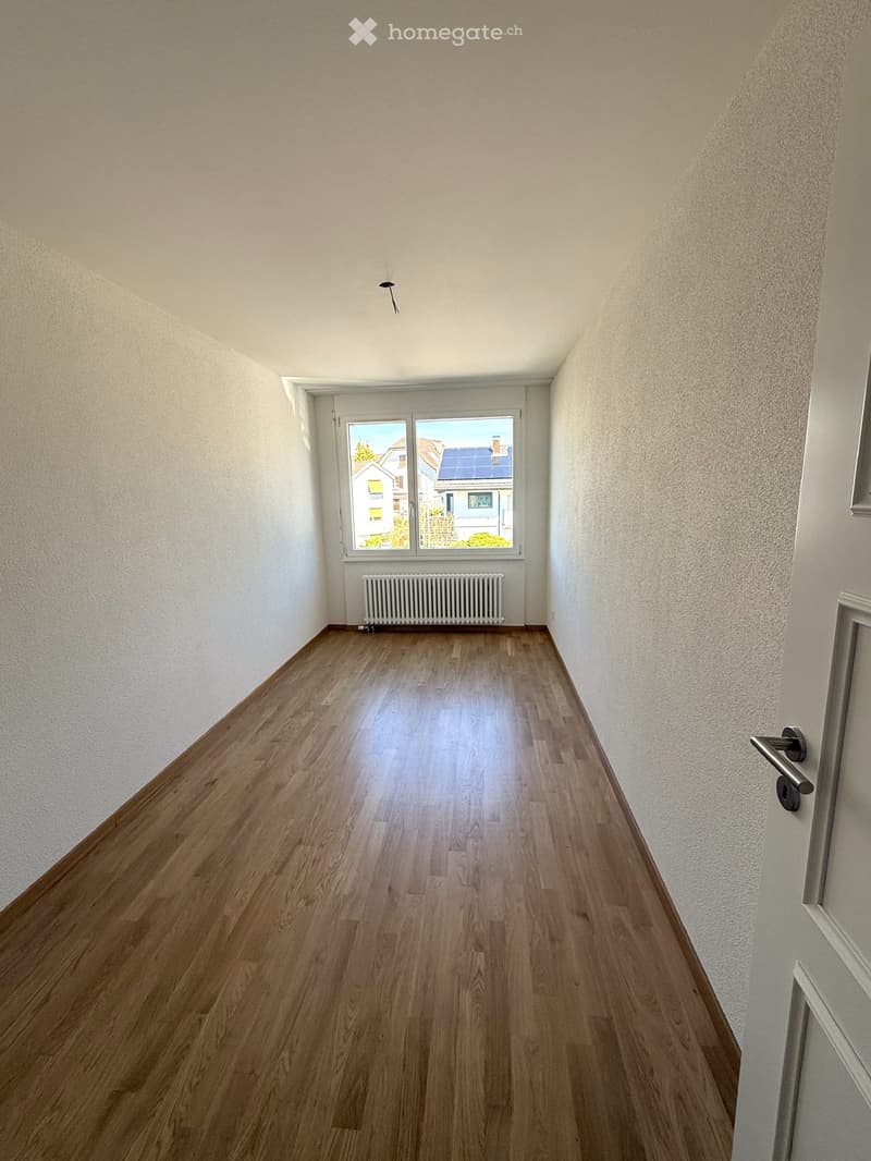 Empty room with wooden floor, white walls, large window, white radiator