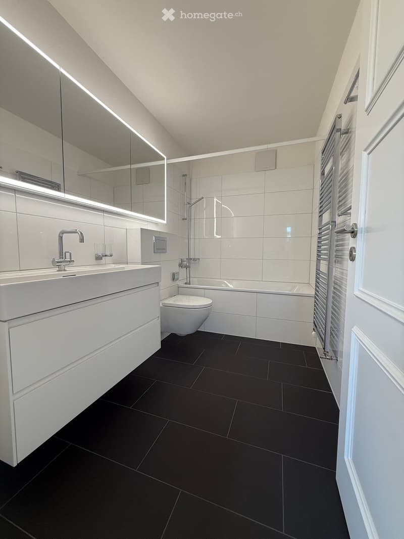 modern bathroom with white tiles, black floor, white vanity, silver faucet, white toilet, bathtub, towel rack