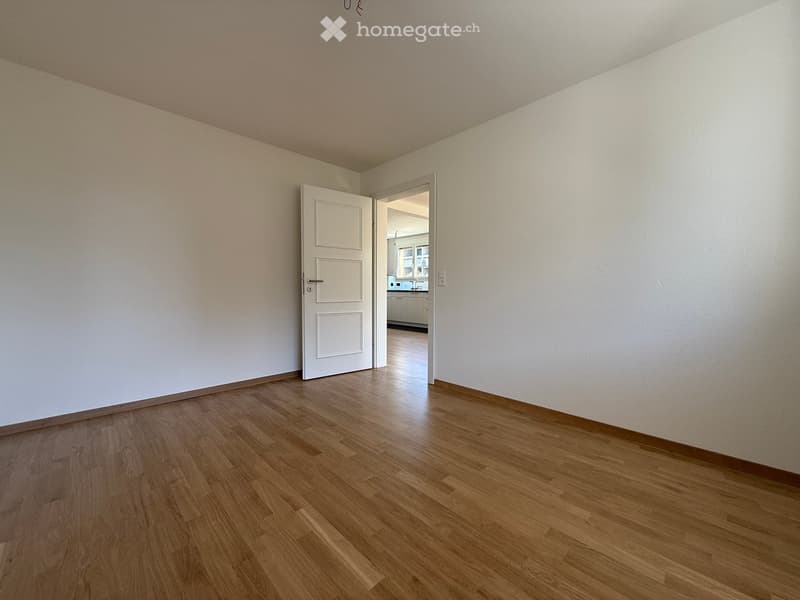Empty room with white walls, wooden floor, open door leading to another room