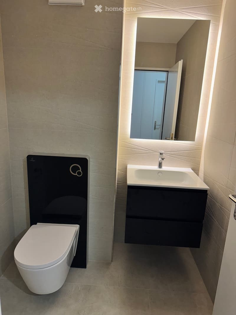 modern bathroom with white toilet, black vanity, white sink, large mirror, tiled walls