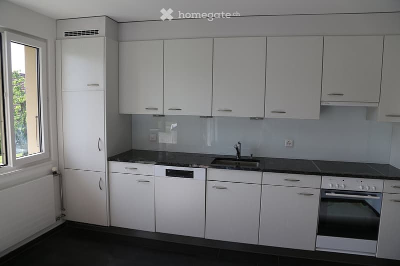 Modern kitchen with white cabinets, black granite countertops, built-in appliances including a dishwasher, and a large window providing natural light.