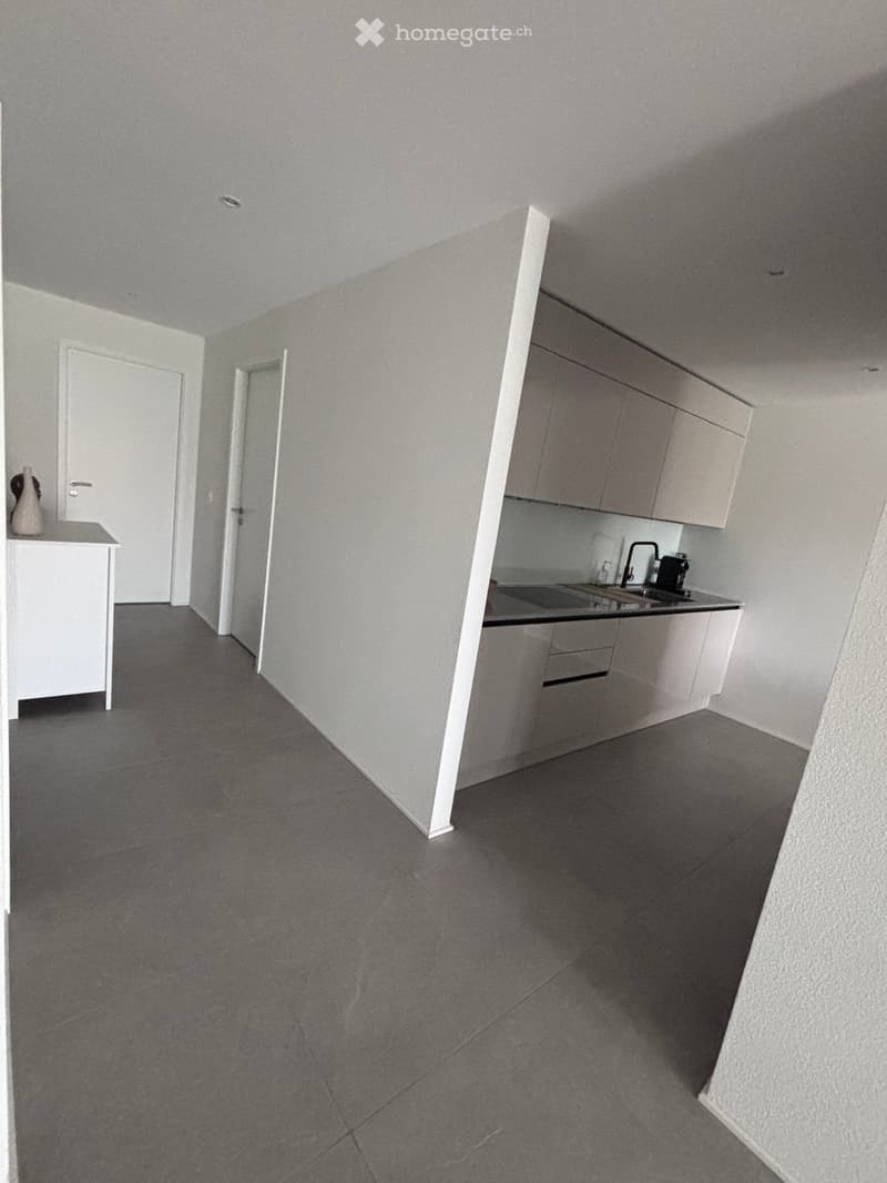 Empty kitchen with grey tiled floor, white cabinets, and a sink area. No furniture or appliances visible.