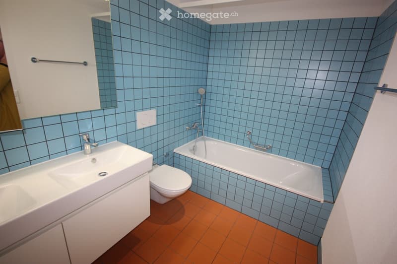 Modern bathroom with blue tiled walls, a white sink, toilet, bathtub, and a mirror above the sink.