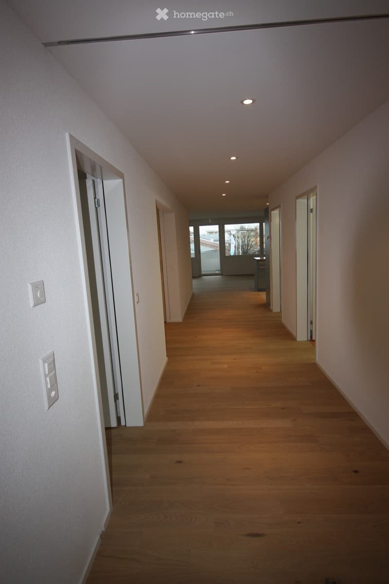 Empty hallway with wooden flooring, white walls, and recessed lighting. Doors are visible on both sides, leading to other rooms.