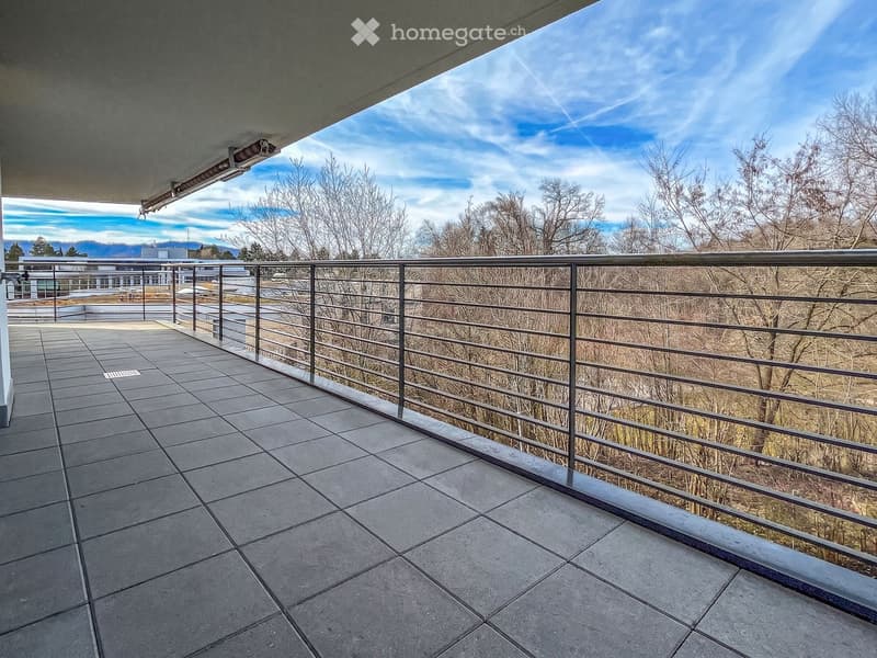 Balcony with tiled floor, metal railing, and scenic view of trees and mountains under a partly cloudy sky.