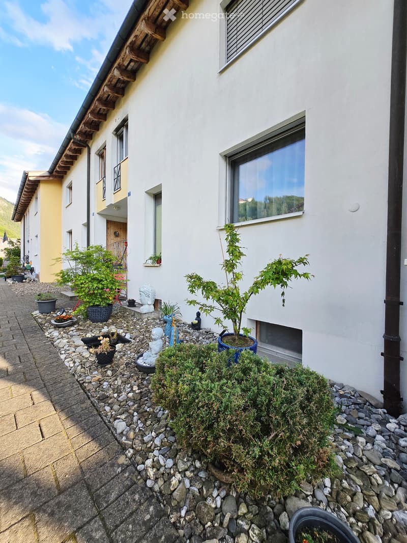 Garden / Outdoor Area. A small garden area with potted plants, rocks, and decorative statues, adjacent to a white building with large windows and a wooden door.