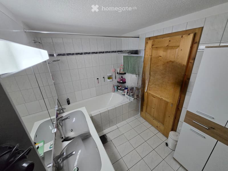 Bathroom. Bathroom with a bathtub, sink, mirror, and shower area. The room features tiled walls and floor, a wooden door, and a small cabinet with drawers.