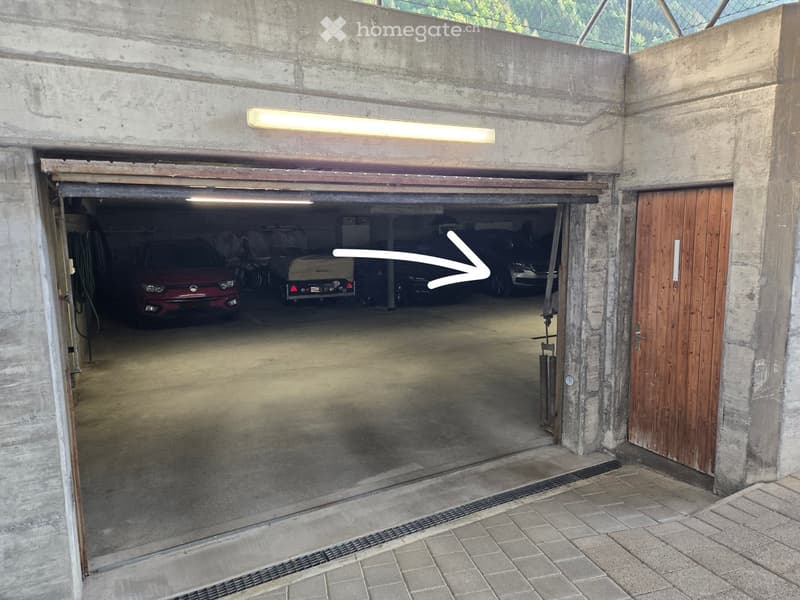Building. Underground parking area with concrete walls, multiple parked cars, and a wooden door on the right side.