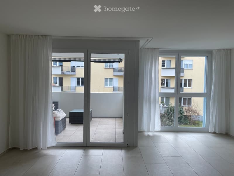 Empty room with large sliding glass doors leading to a balcony, white tiled floor, and white curtains on the windows.