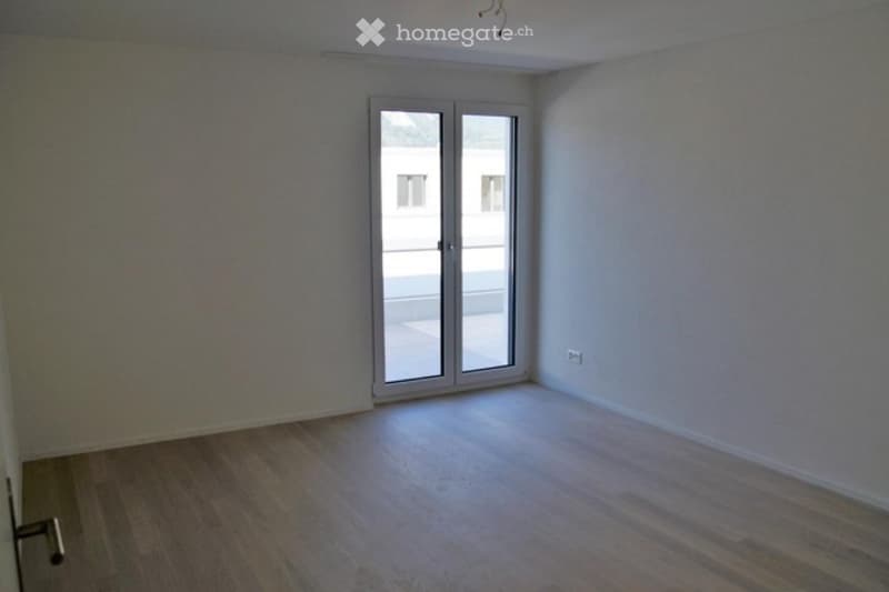 Empty room with wooden flooring, white walls, and a large sliding glass door leading to a balcony.