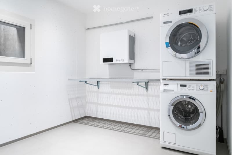 A clean and simple room with white walls and a floor, a washer and dryer, and a shelf with an attached dehumidifier.