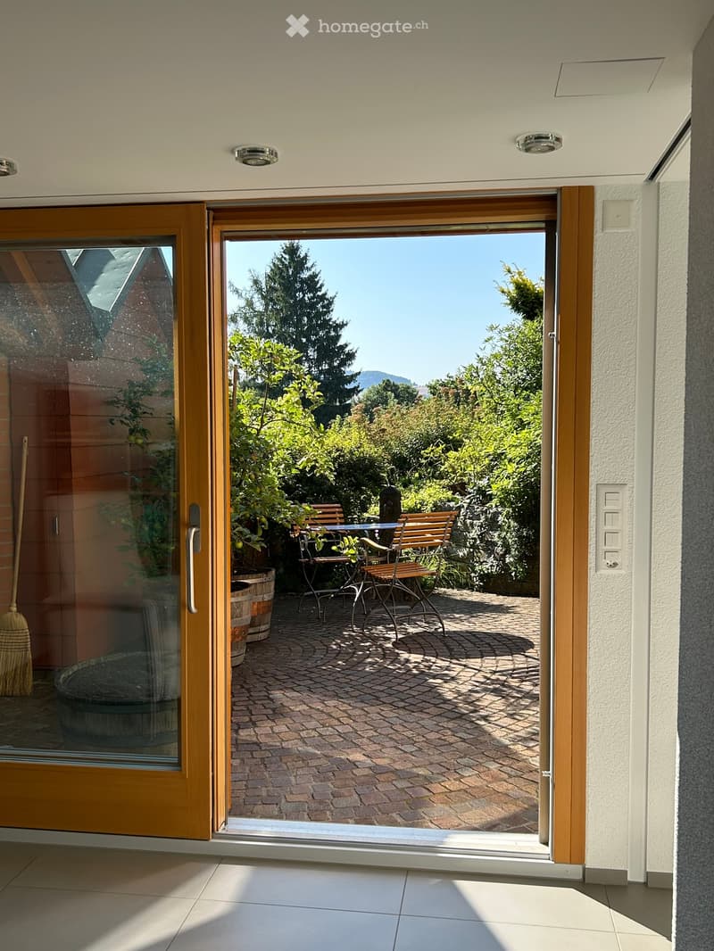 Sliding door leading to a patio with a brick floor, table, and chairs, potted plants, and a garden view