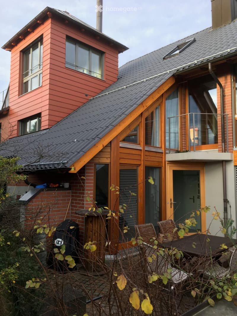 House with brick exterior, modern architecture, wooden balcony, and a red facade on the upper level.