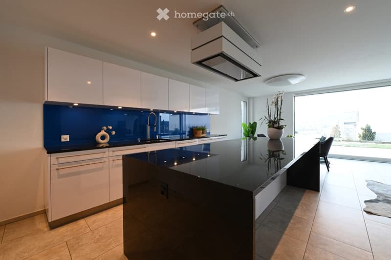 Kitchen. Modern kitchen with white cabinets, black countertops, a central island, and a sink with a modern faucet. The space features a sleek design with a blue backsplash and ample natural light from large windows.