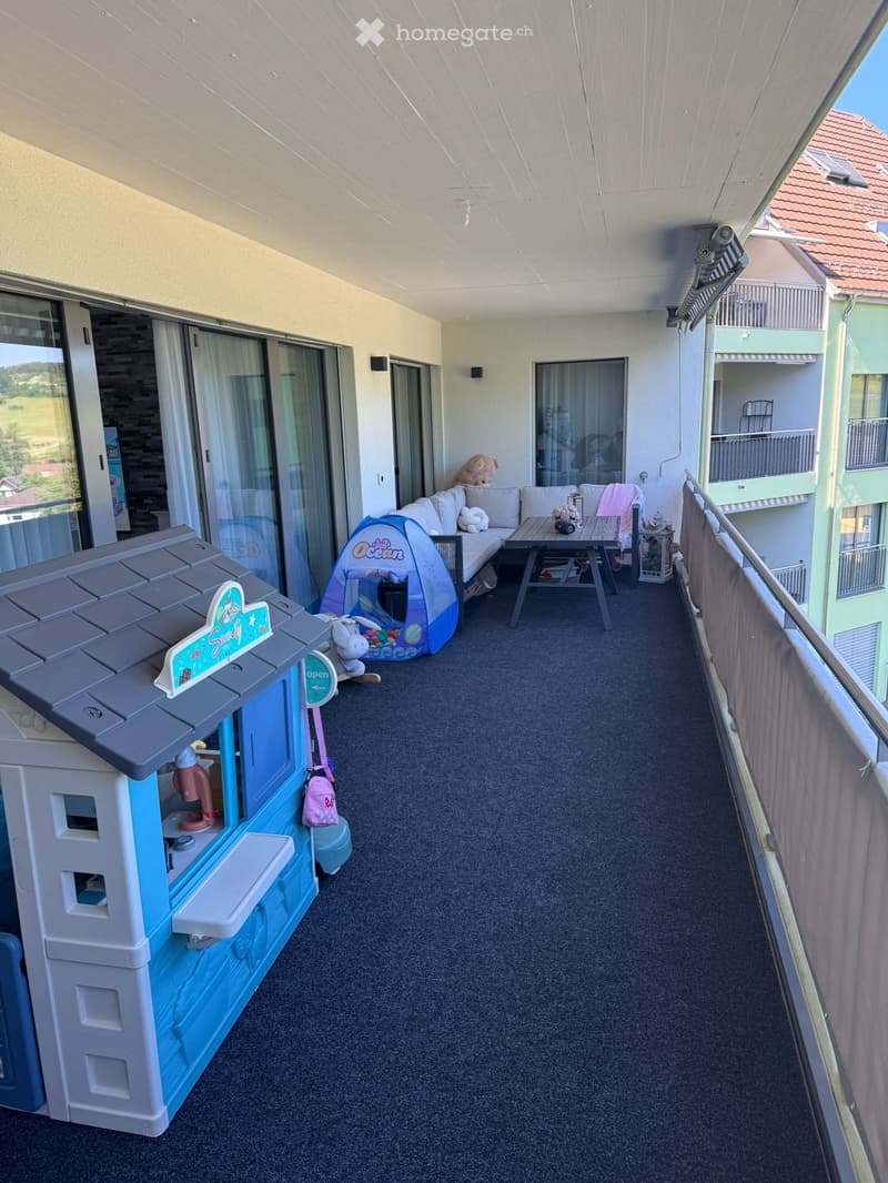 Balcony with carpeted floor, sofa, small table, toy house, tent, and stuffed animals.